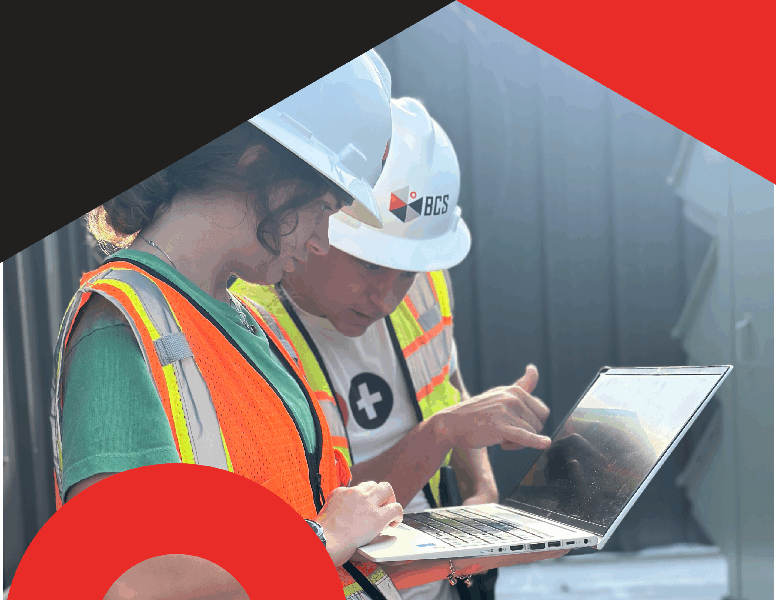 Two HVAC controls engineers in safety vests and hard hats review building system data on a laptop on a building's rooftop.